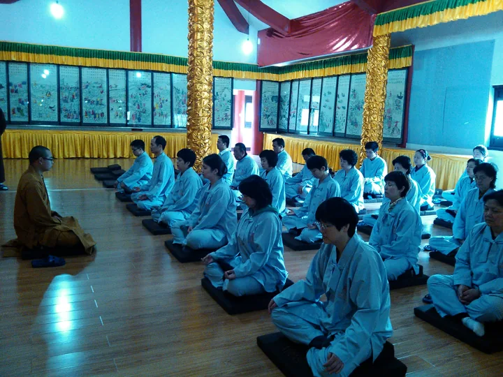 Participants sit in rows on cushions inside a temple meditation hall.