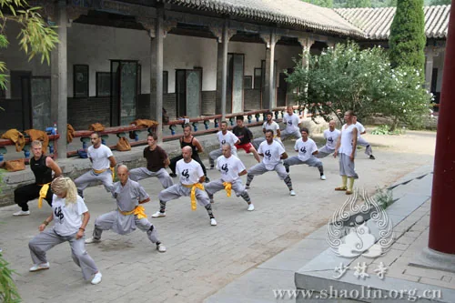 Students in light grey training clothes practise in a courtyard.