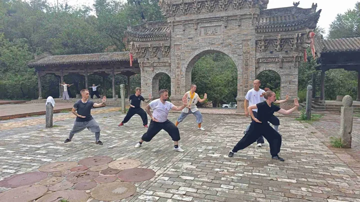 Students practise martial-arts stances in a stone courtyard.