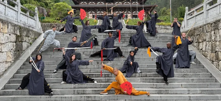 A retreat group poses with swords, spears and fans on broad temple steps.