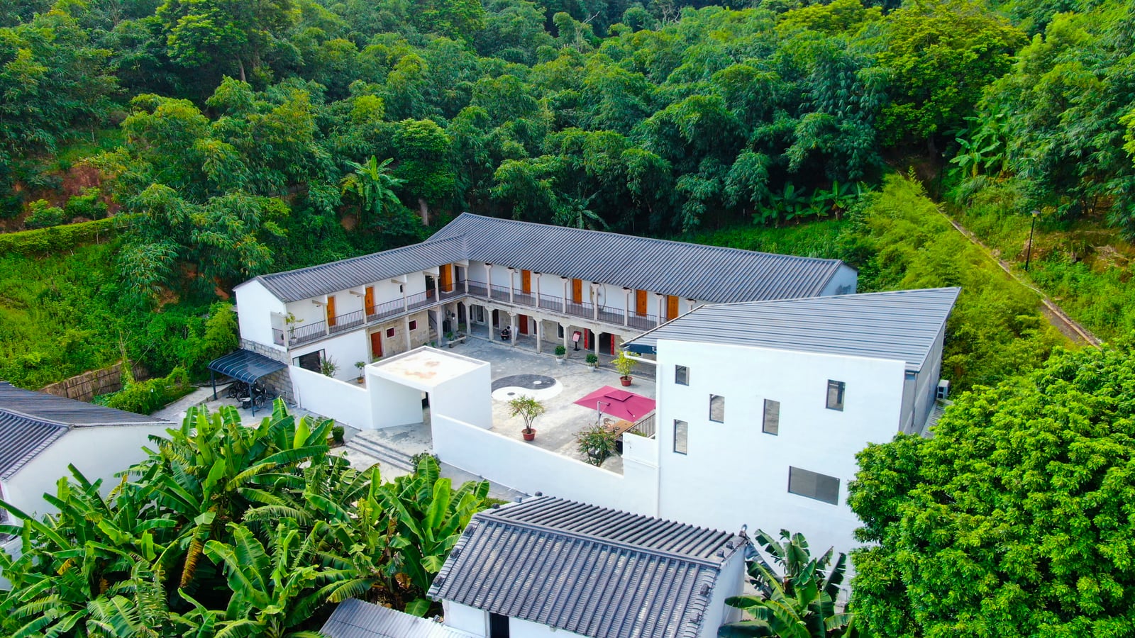 White courtyard buildings among bamboo and forest, seen from above.