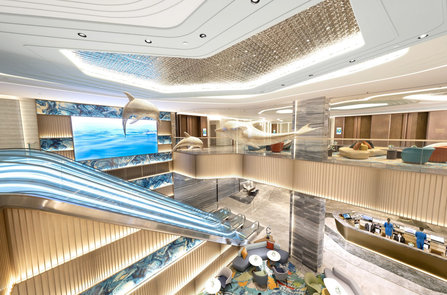 Atrio del Regala Skycity Hotel con scale mobili, sculture di delfini e reception con personale.