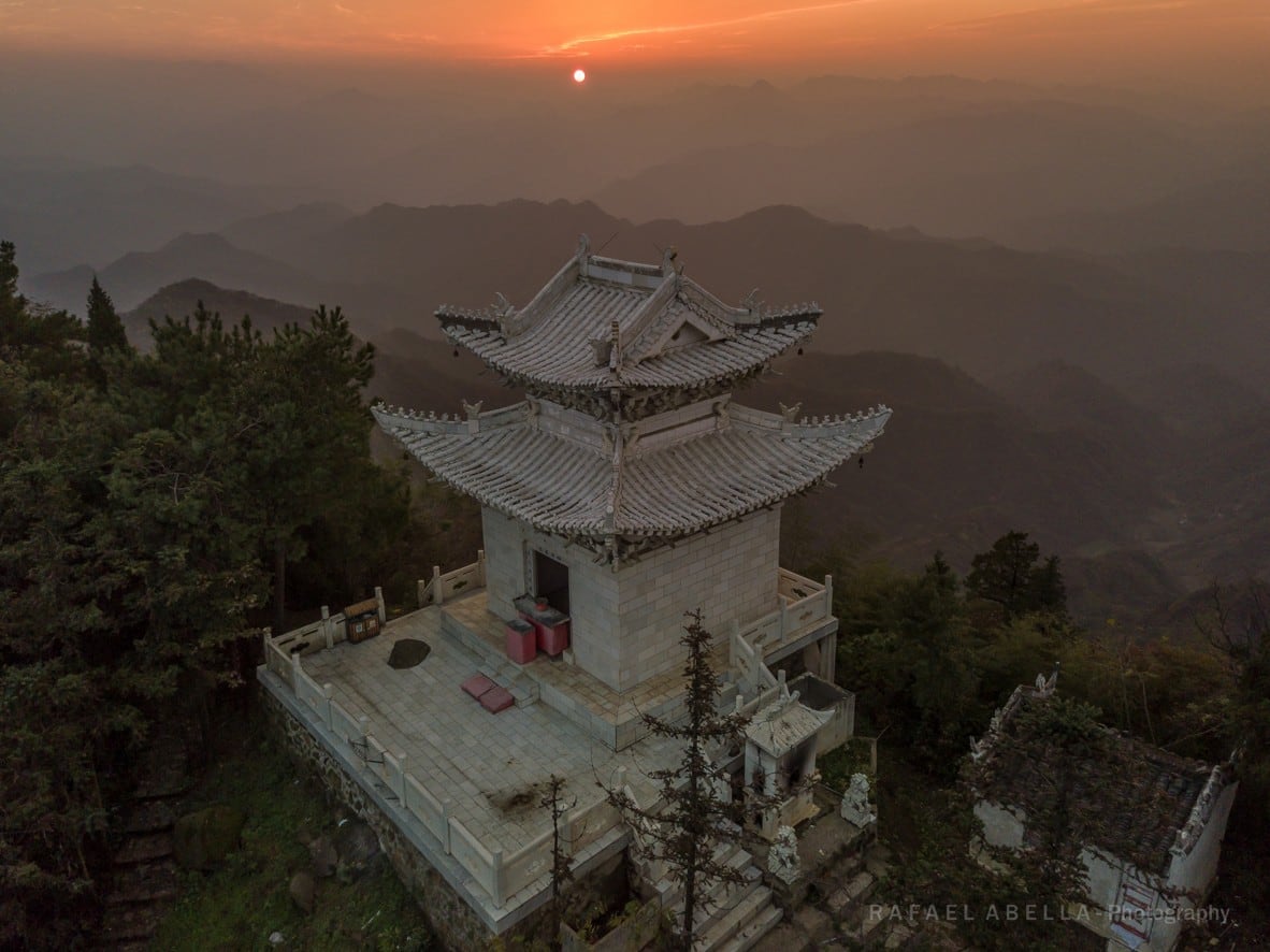 Un piccolo tempio bianco su una vetta all’alba, con crinali a strati alle spalle.