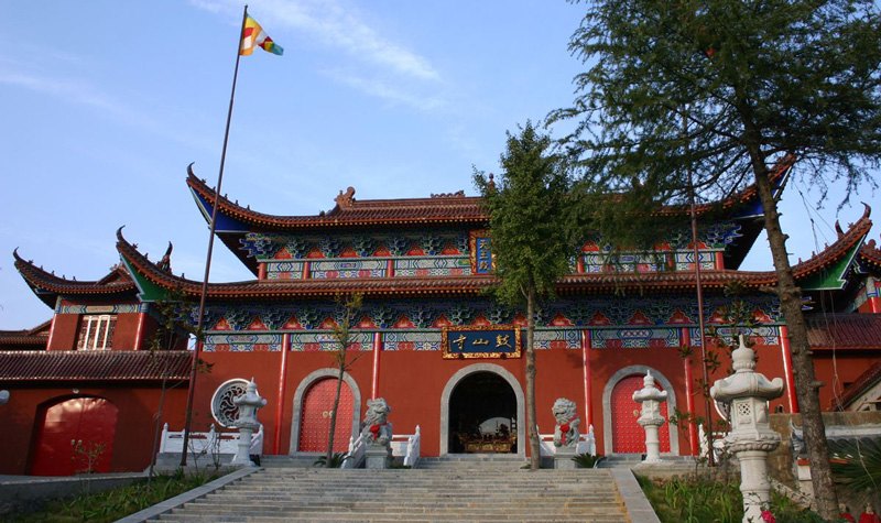 Porte de temple rouge aux avant-toits ornés, marches en pierre et lions gardiens.