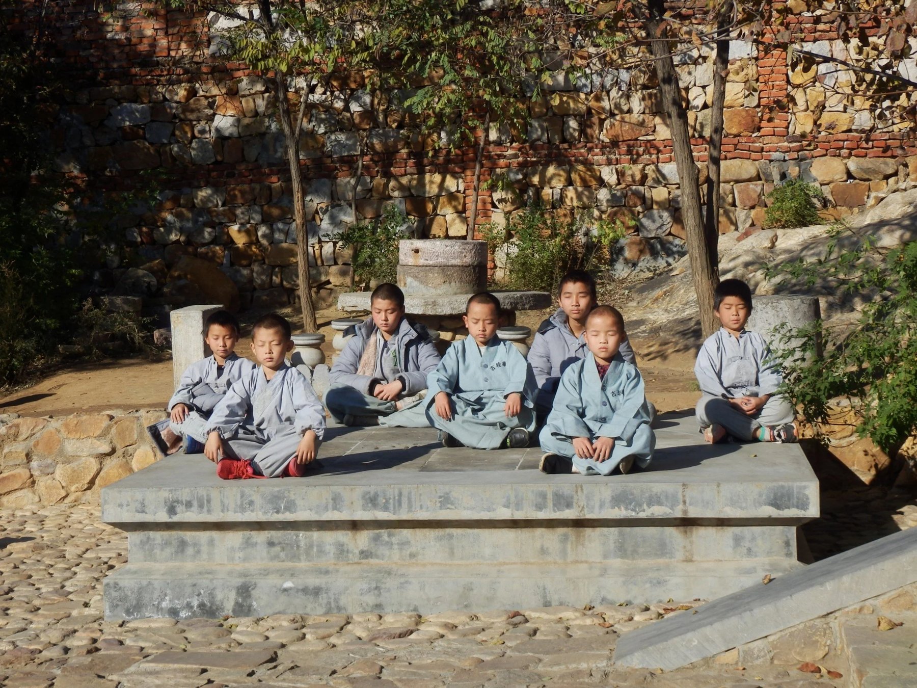 Children and an instructor sit in a stone courtyard.