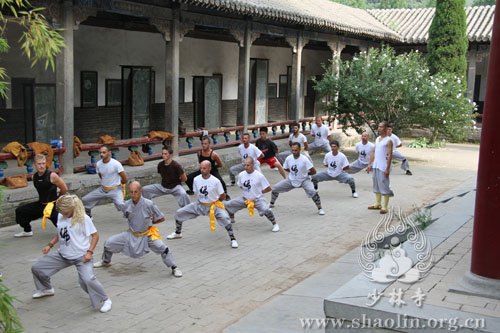 Students in light grey training clothes practise in a courtyard.