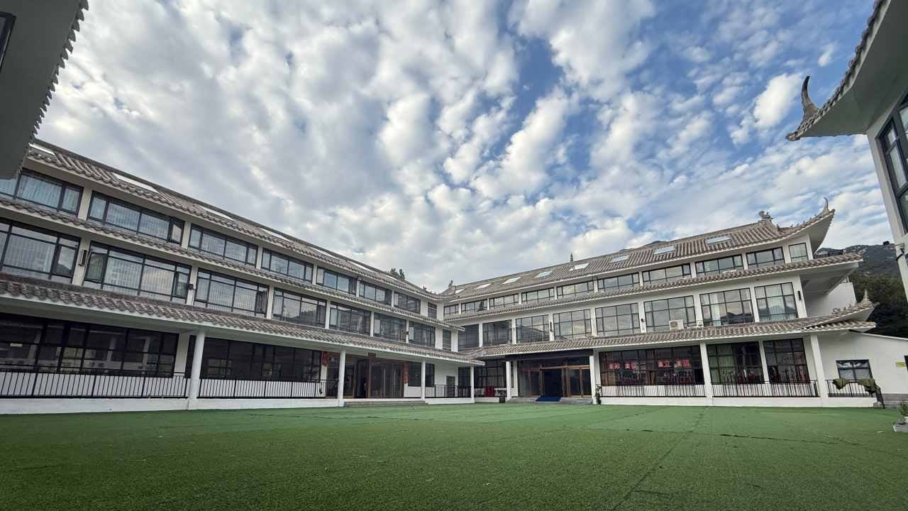 A three-storey grey-tiled courtyard building around a green lawn.