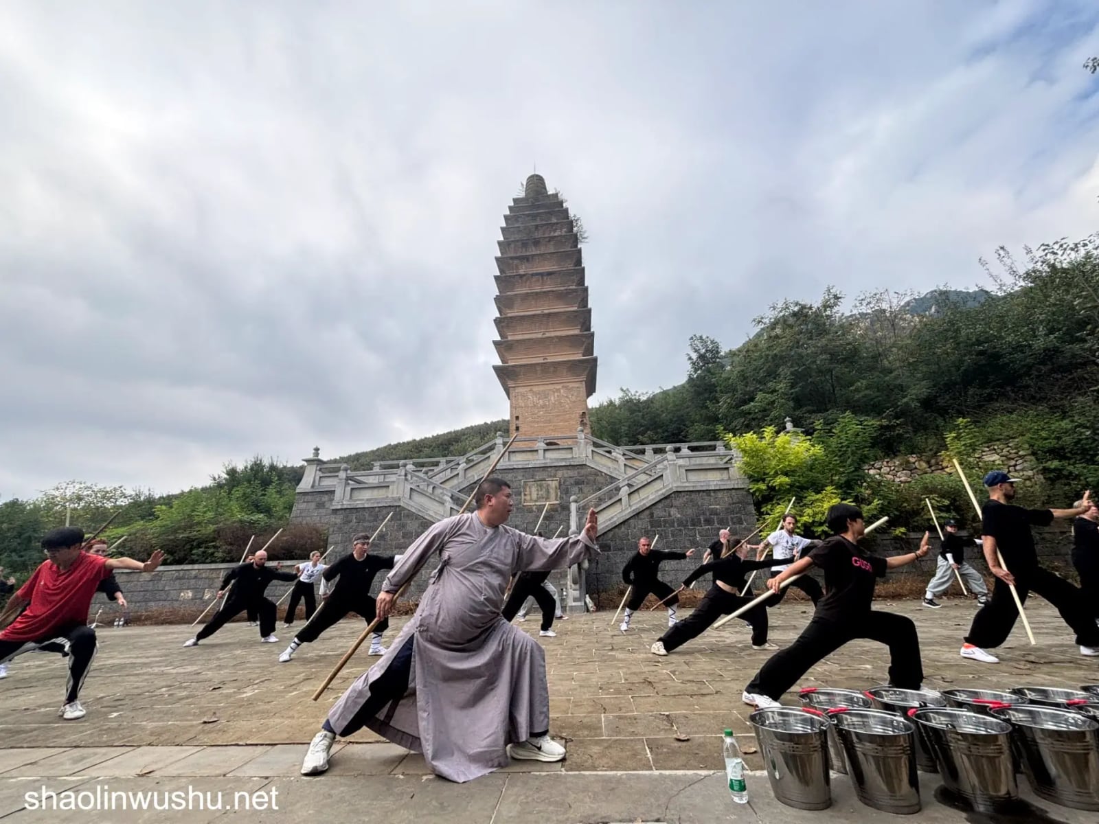 A monk-robed teacher leads staff practice below a brick pagoda.