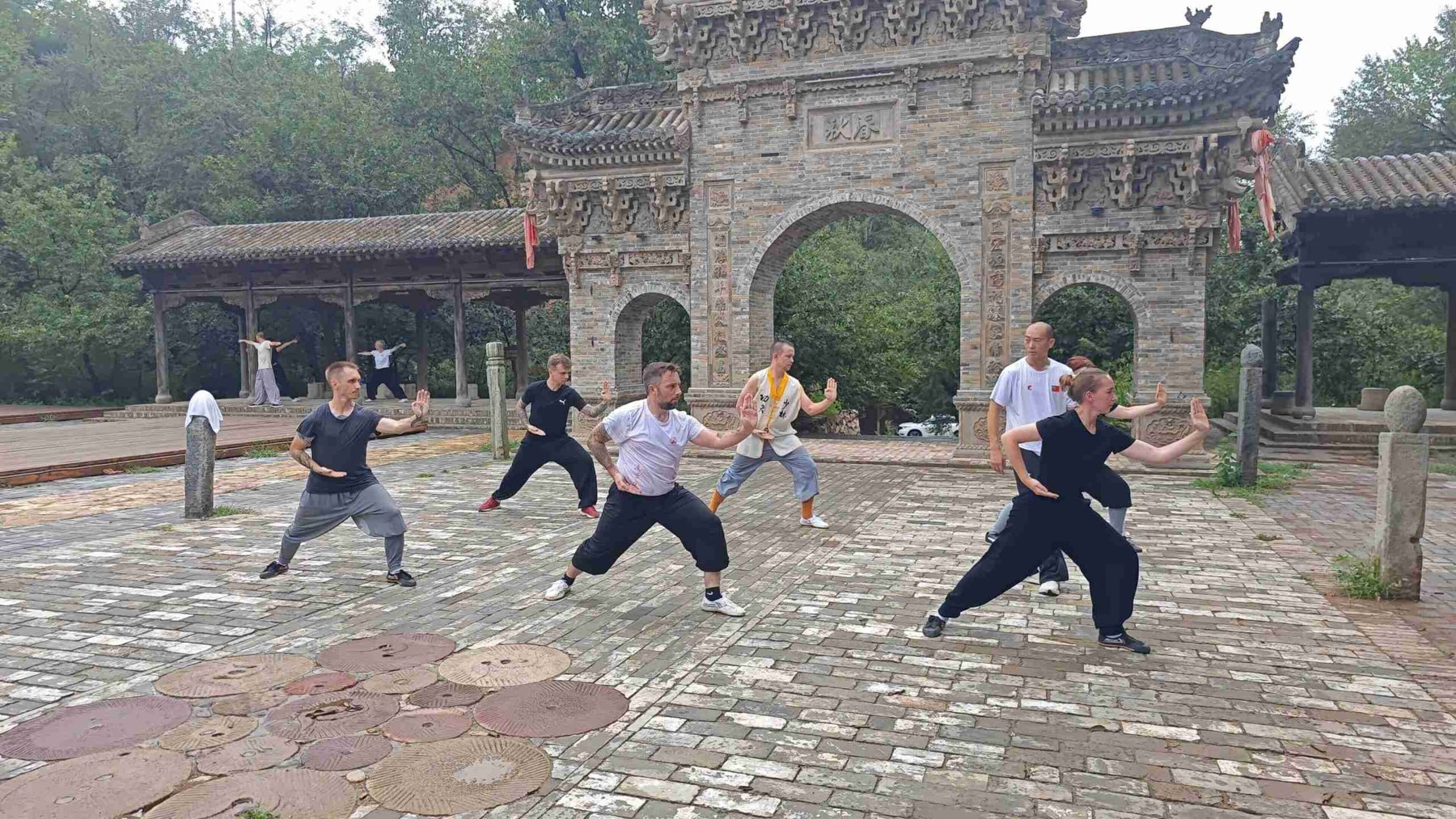 Alumnos practican posturas de artes marciales en un patio de piedra.