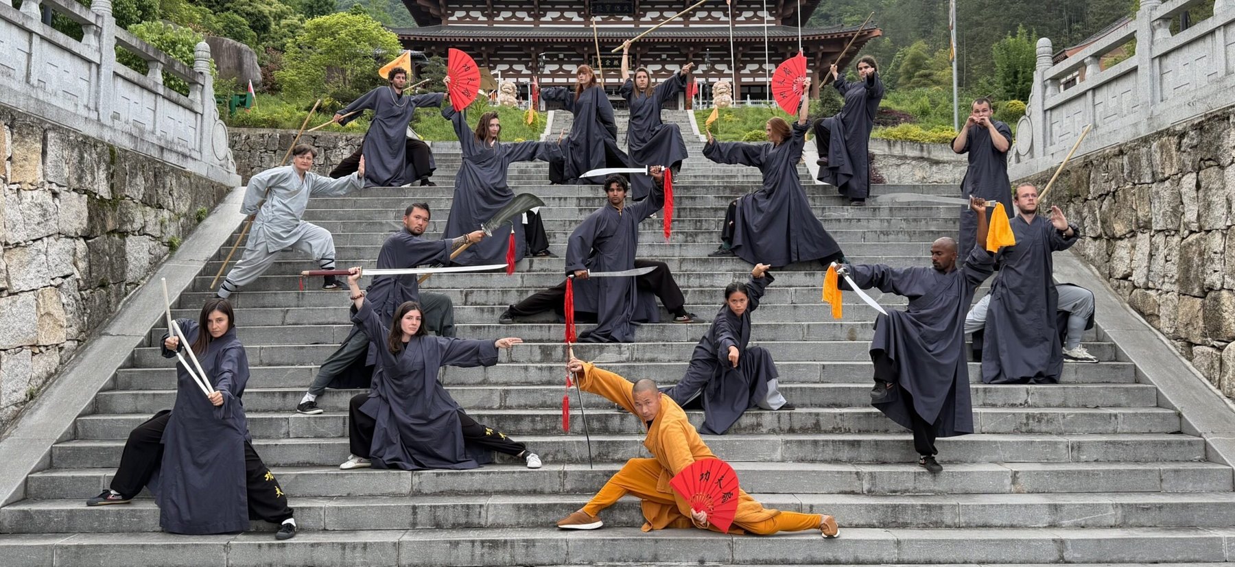 A retreat group poses with swords, spears and fans on broad temple steps.