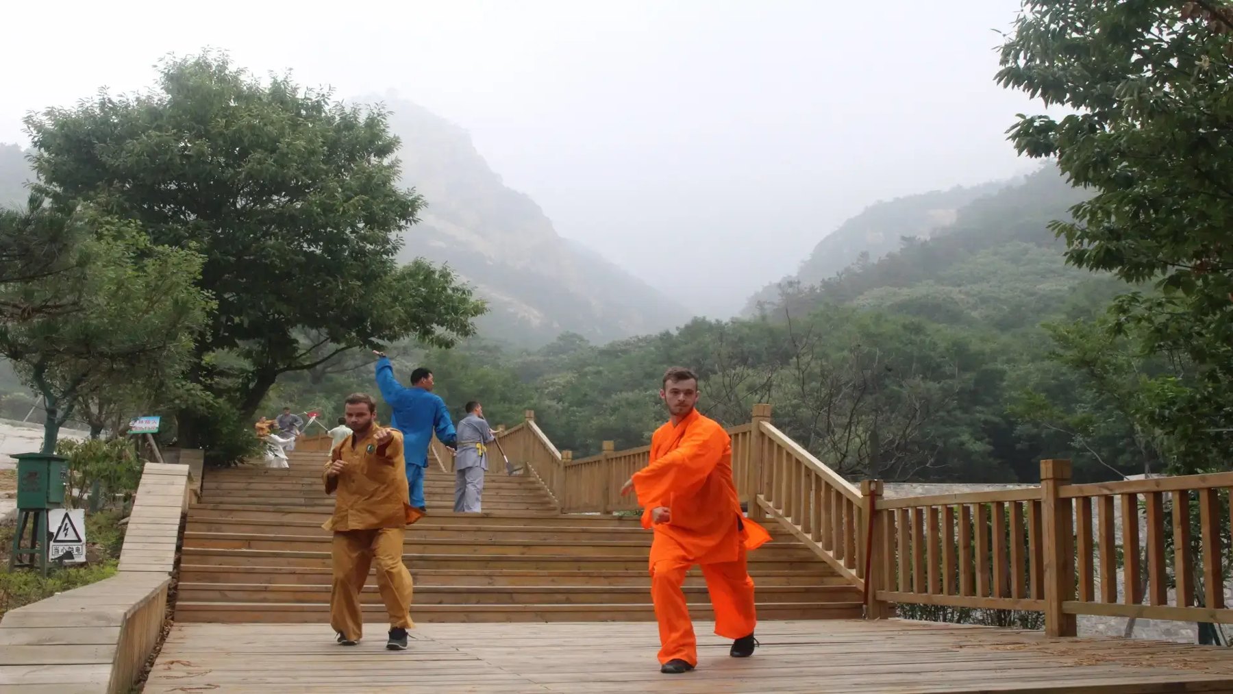 Un enseignant en orange et des élèves pratiquent sur une terrasse de montagne.