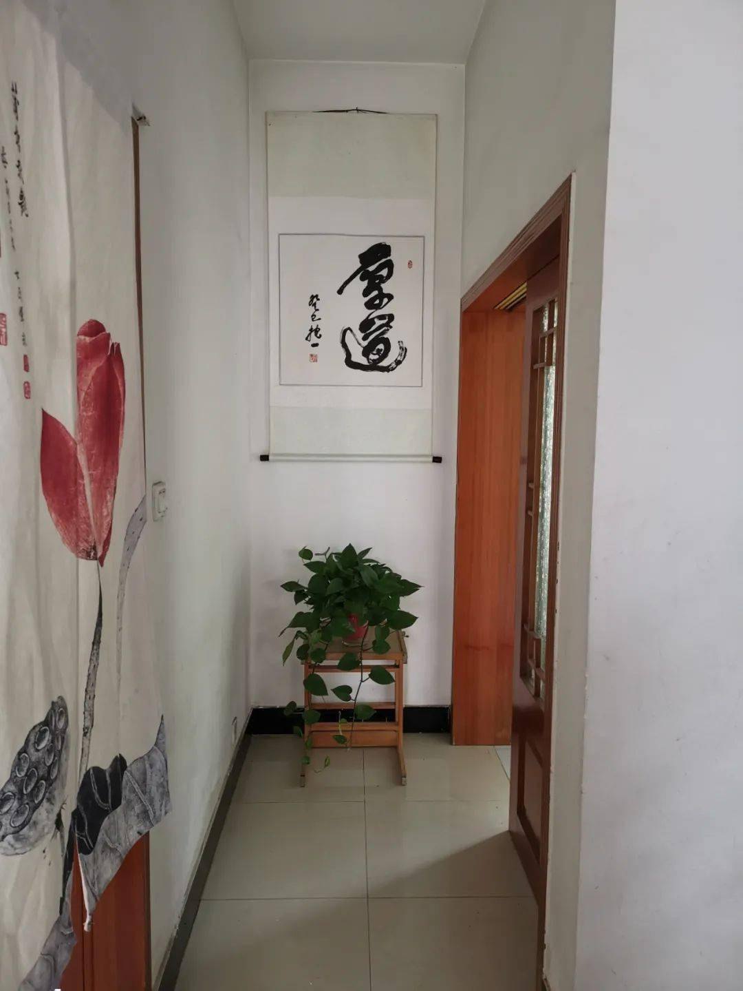 Pasillo blanco estrecho con decoración de loto, caligrafía y una planta en maceta.