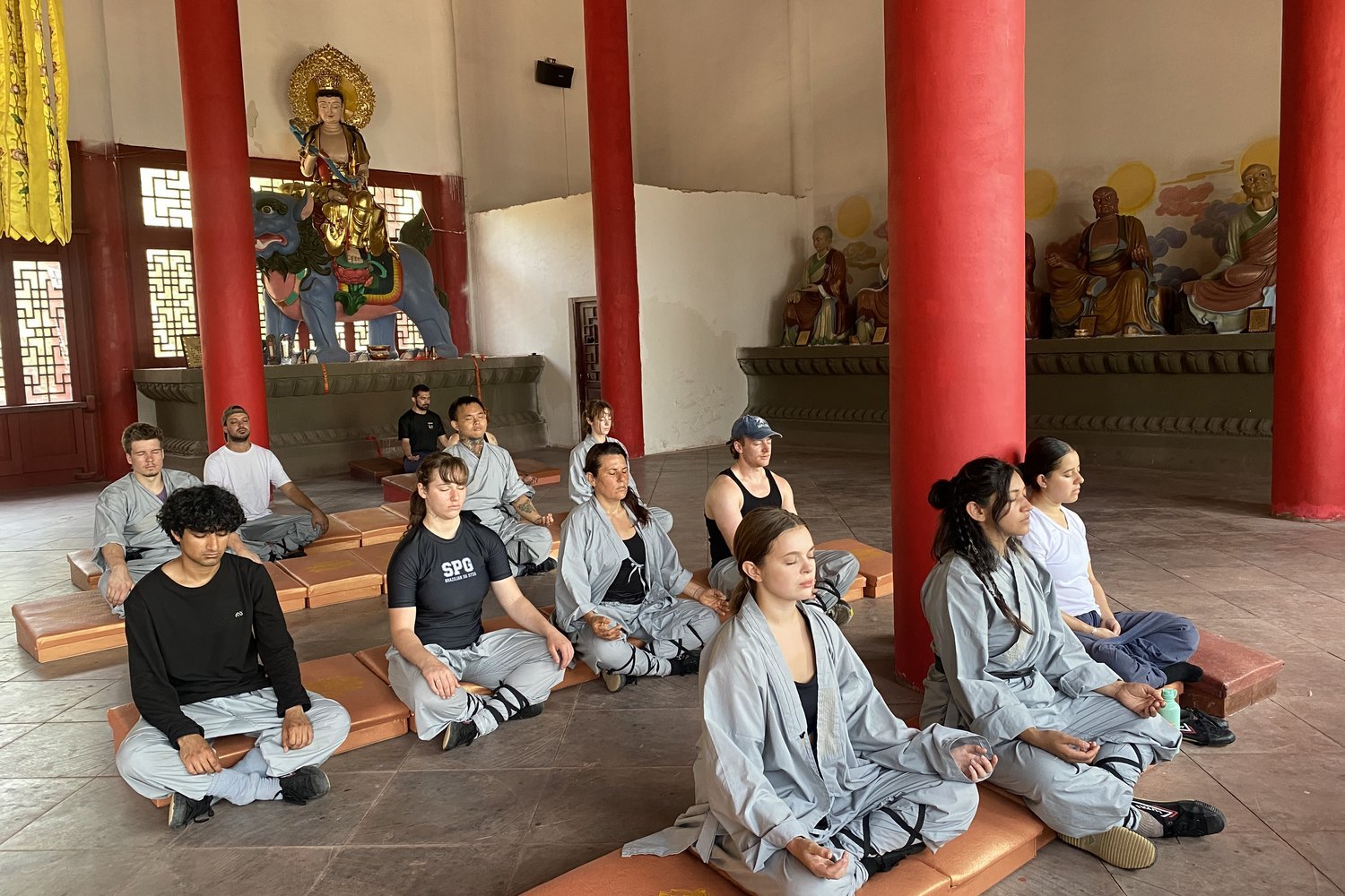 Students sit cross-legged inside a temple hall with red columns.