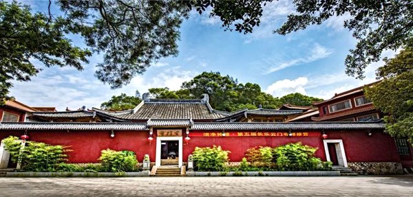 浓密树叶下长长的红色寺墙与山门。